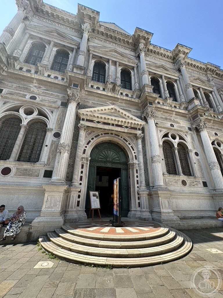 The marble front of the Scuola Grande di San Rocco in Venice, its paired Corinthian columns above a semicircular flight of steps at the portal