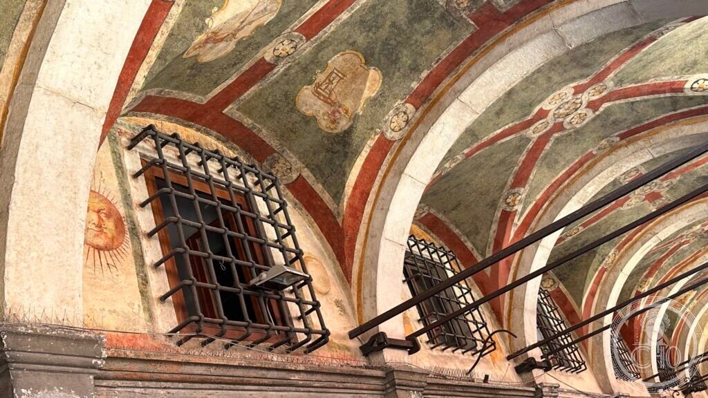 Detail of a cross vault with worn painted decoration, a barred window set into it