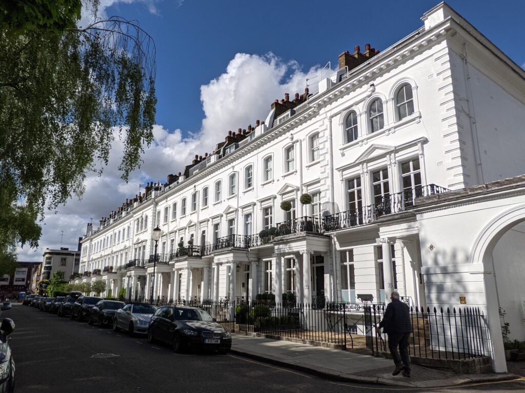 White stucco terrace at 13-23 Sumner Place, South Kensington, with columned porches, a continuous iron balcony and arched top-floor windows on the end house