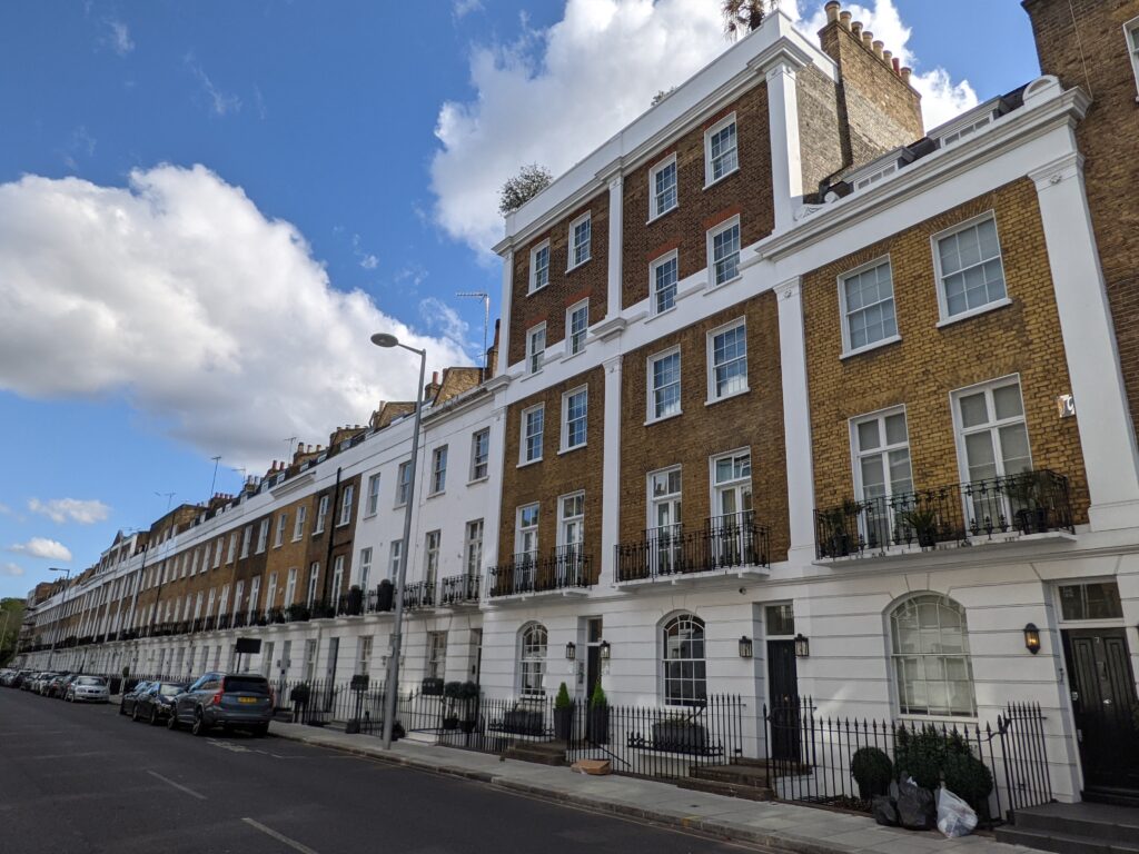 Listed terrace at 7-67 Sydney Street, Chelsea: yellow stock brick upper floors over a white stucco ground floor, with individual iron balconies and white pilaster strips