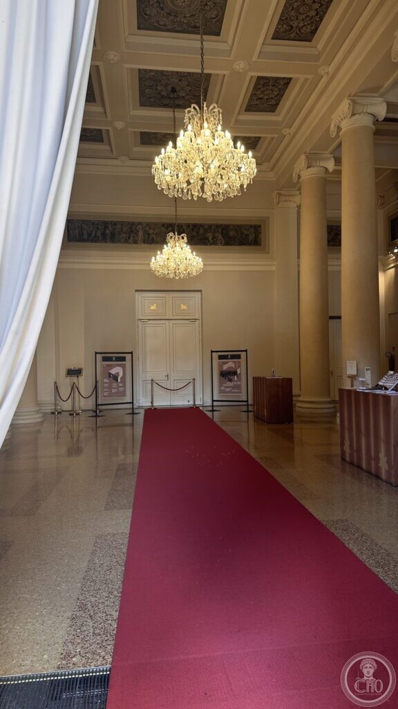 The theatre foyer with two crystal chandeliers, columns, a coffered ceiling and a red carpet