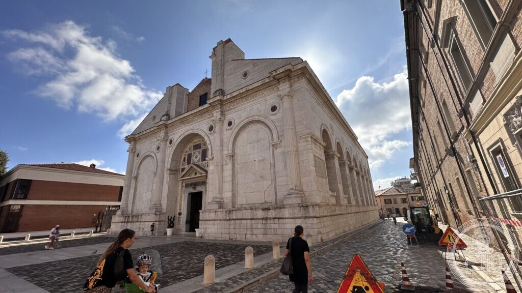The white marble front of the Tempio Malatestiano with the arcaded side wall running away to the right