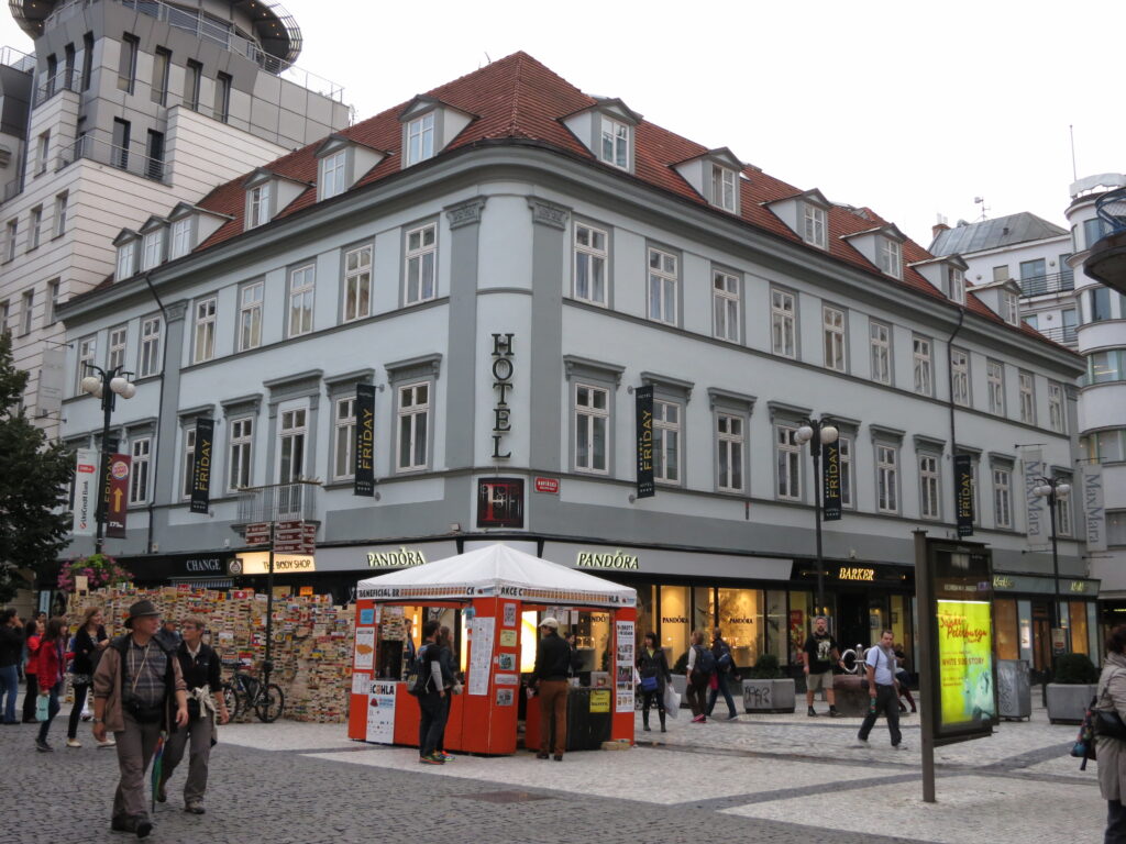 Pale grey-green classicist corner house with red tiled roof and dormers on Na Příkopě in Prague, with shops on the ground floor