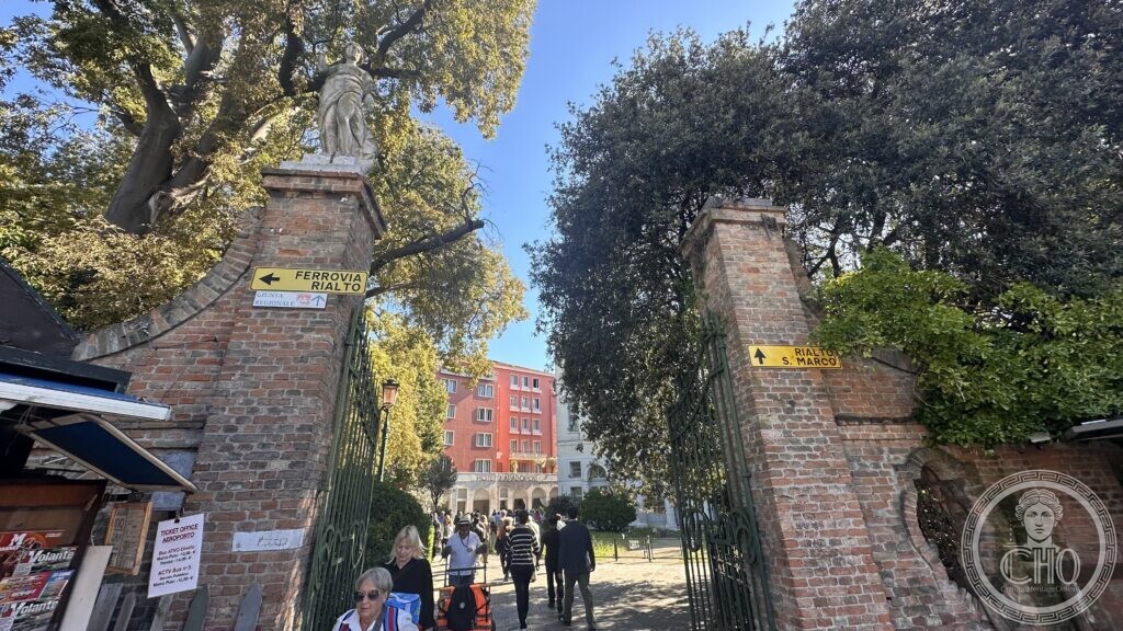 Brick gate pillars with statues and yellow direction signs, a hotel and trees behind