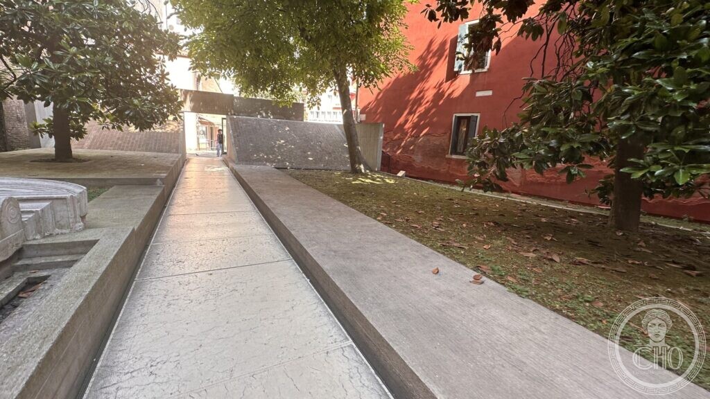The courtyard of the Iuav at the Tolentini: a paved path between the portal basin and a lawn under magnolias, leading to the university entrance