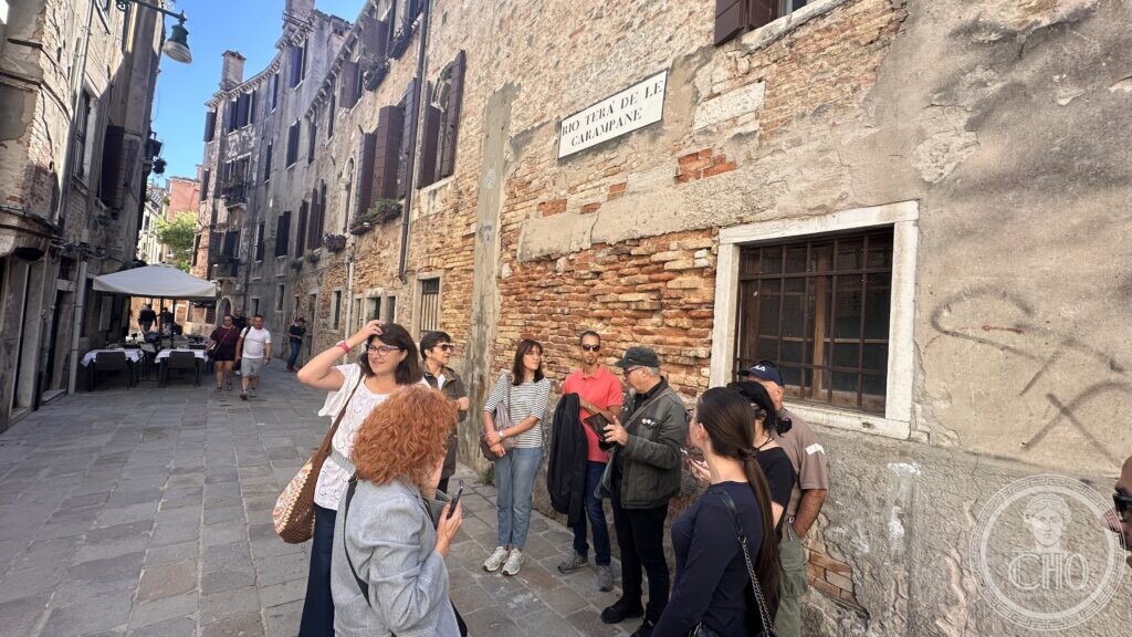 The street sign of Rio Terà de le Carampane on a brick wall, with the walking group beside it
