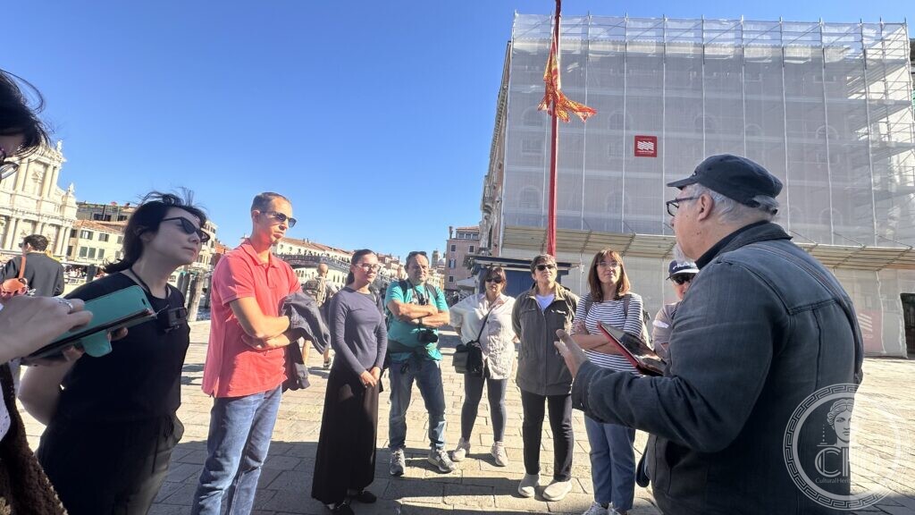A group of walkers in a Venetian campo, one of them speaking with a notebook in his hand