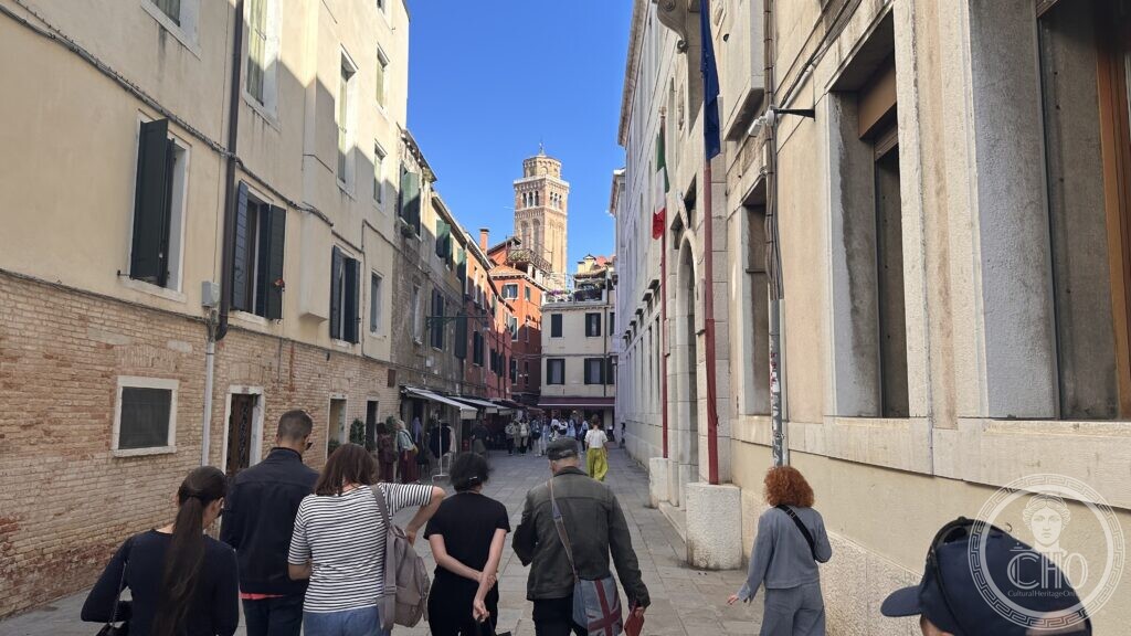 Walkers in a narrow calle with a brick bell tower closing the view at the far end