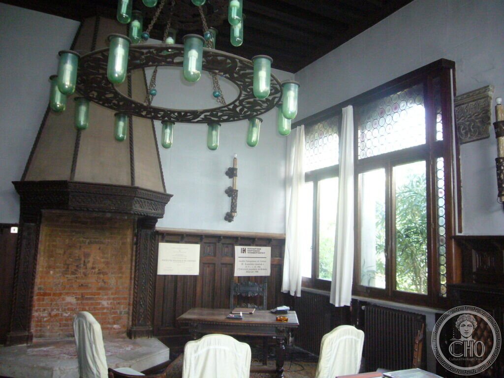 Hall of Villa Hériot with monumental hooded fireplace, carved wood panelling and wrought-iron chandelier with green glass lamps