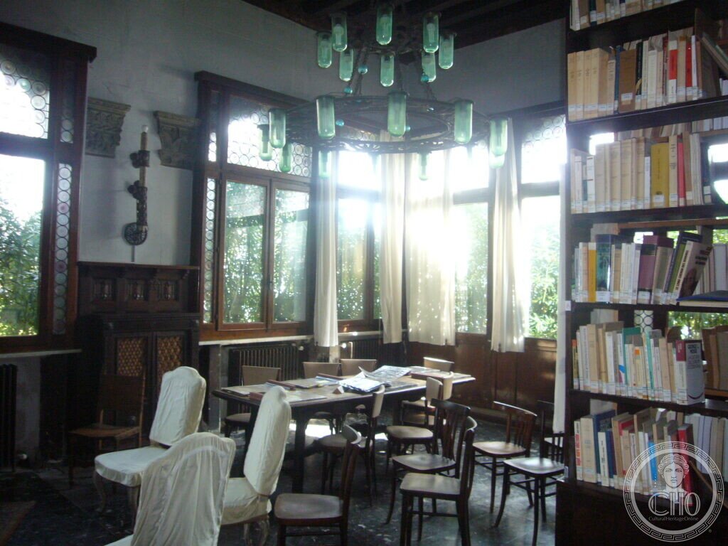 Reading room inside Villa Hériot with bookshelves, reading table and iron chandelier with green glass lamps