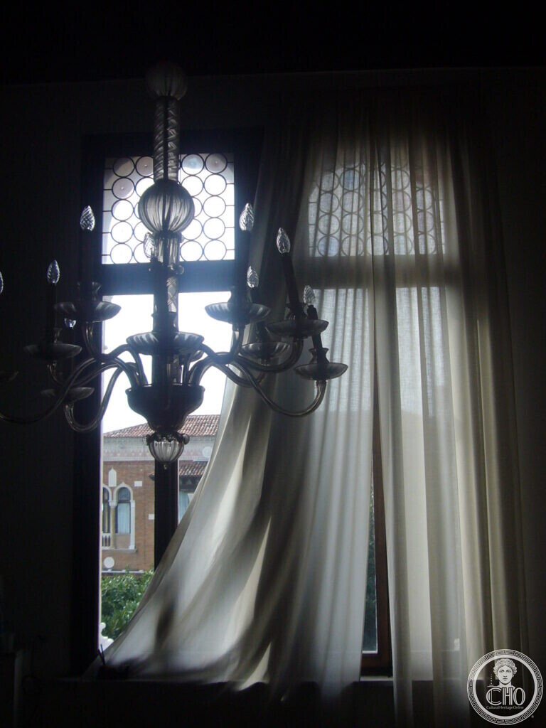 Murano glass chandelier silhouetted against a window with circular leaded panes inside Villa Hériot