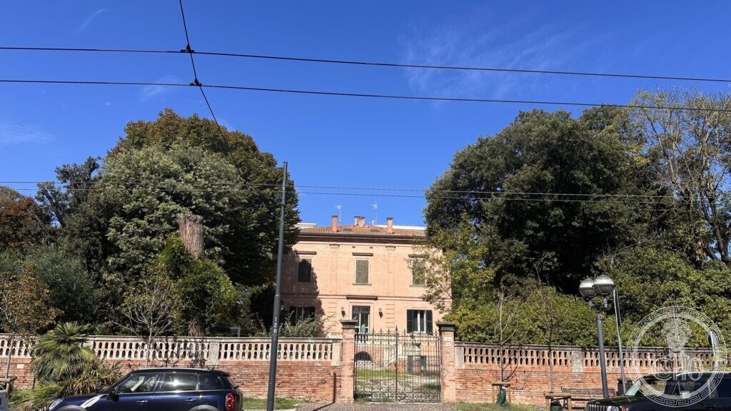 The villa half hidden behind tall dark ilexes, seen from the avenue