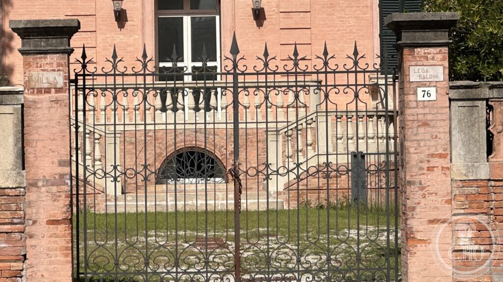 The iron gate of the villa between brick pillars carrying marble tablets reading Villa and Lega Baldini 76