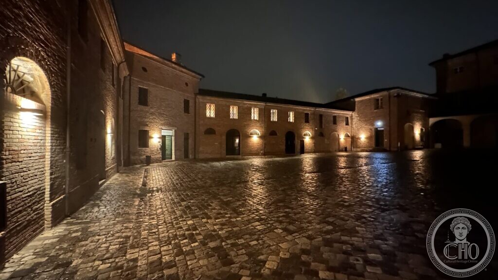 The lit arcades of the courtyard ranges at Villa Torlonia, reflected in the wet cobbles