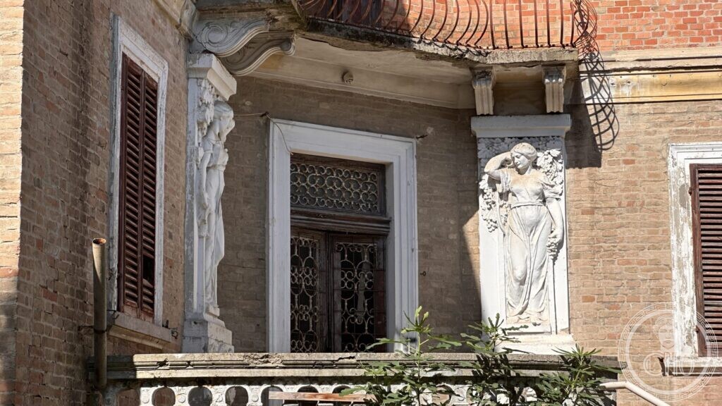 Two carved female figures in white stone flanking a French window under a curved hood