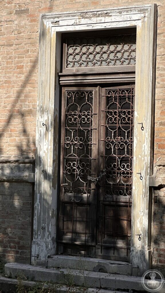 A tall wooden door filled with wrought-iron Art Nouveau scrollwork, chained shut