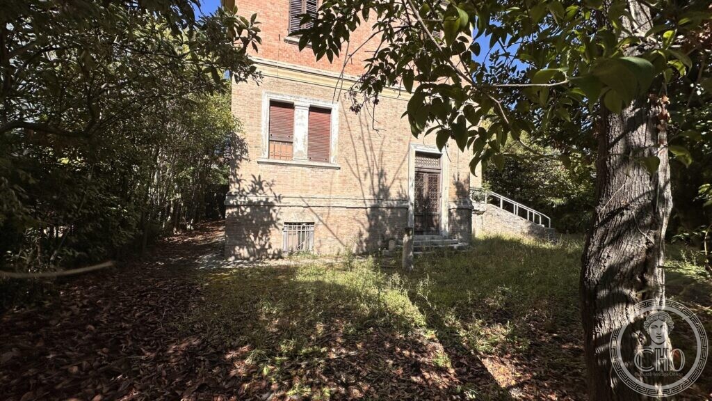 The back of the villa, plain brick with a small door and a barred basement window, grass grown up to the walls