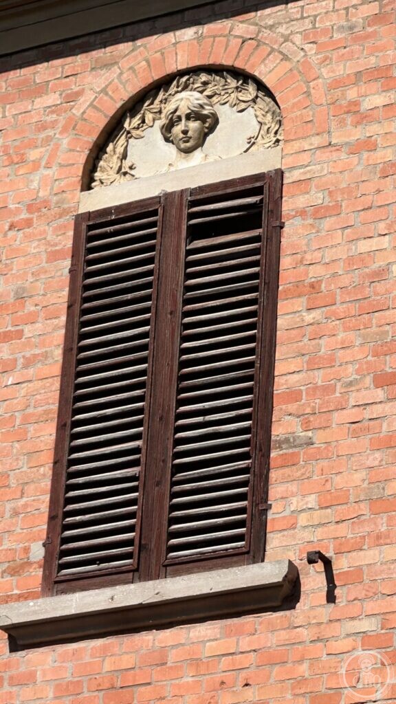 A moulded lunette above a shuttered window with a carved woman's head in a wreath of leaves