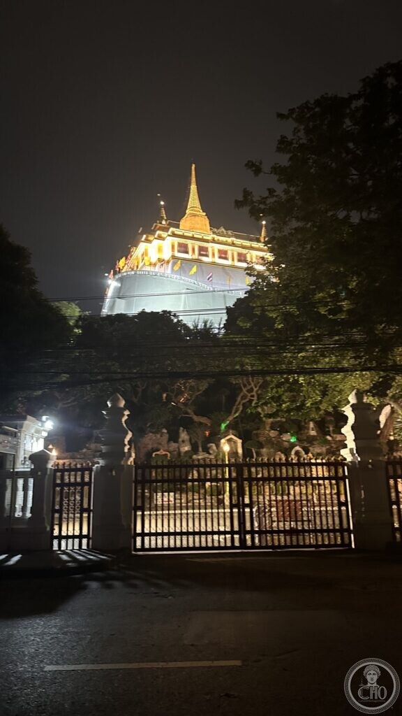 The Golden Mount of Wat Saket seen at night from the street, above the closed iron gates of the temple