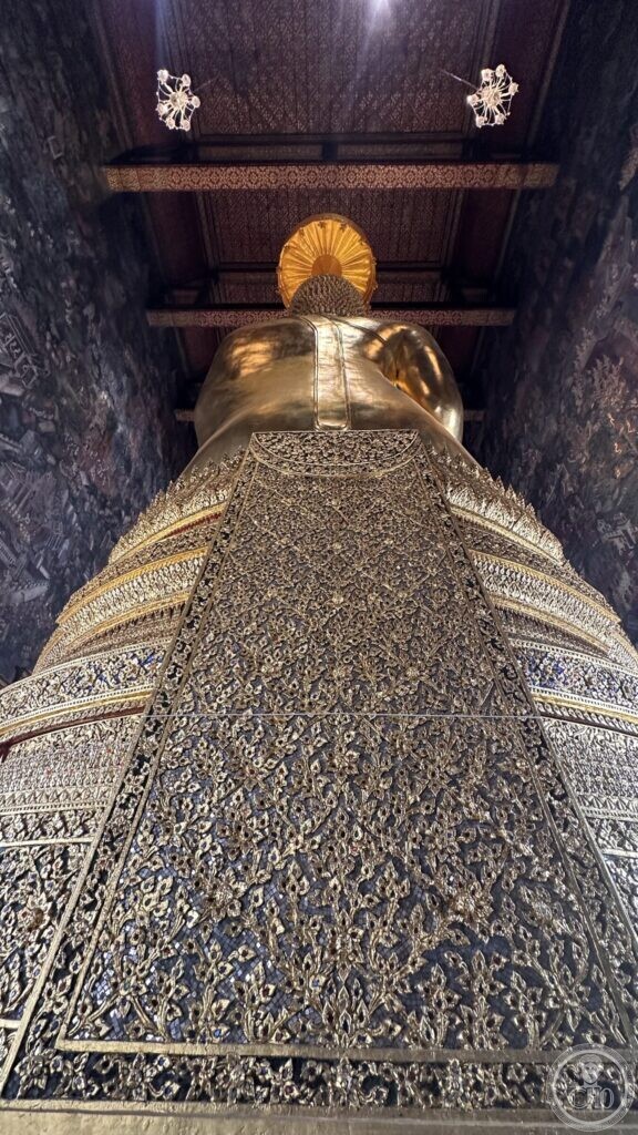 Looking up the length of the Buddha's base at Wat Suthat, sheathed in gilded and inlaid ornament, with the ribbed parasol behind the head and the timber roof above