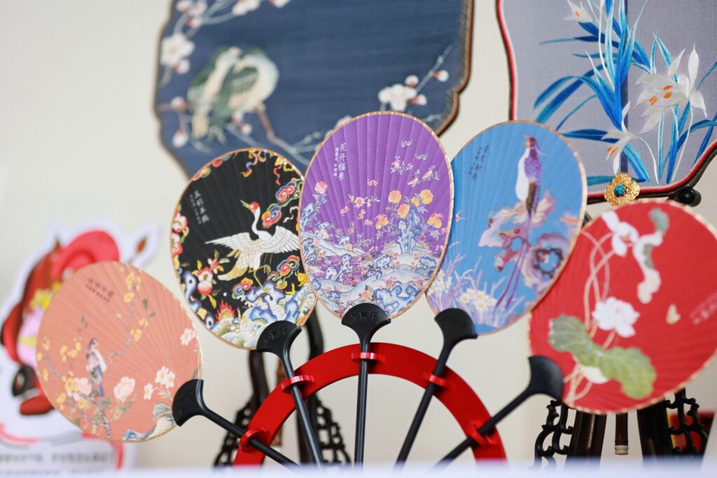 A display of round hand-painted Chinese silk fans with bird and floral motifs, part of the traditional craftsmanship shown at Yu Garden Hamburg
