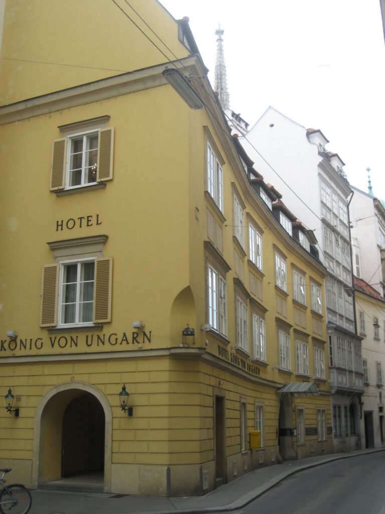 Yellow corner house with a round-arched portal and the painted name König von Ungarn, the spire of St Stephen's behind