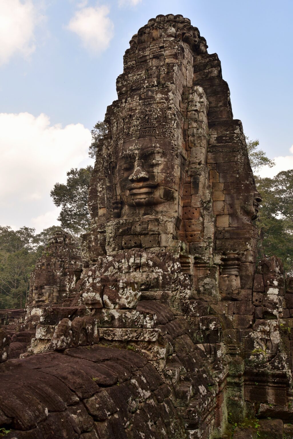 A stone tower of the Bayon carved with a huge serene face, seen from below against the sky