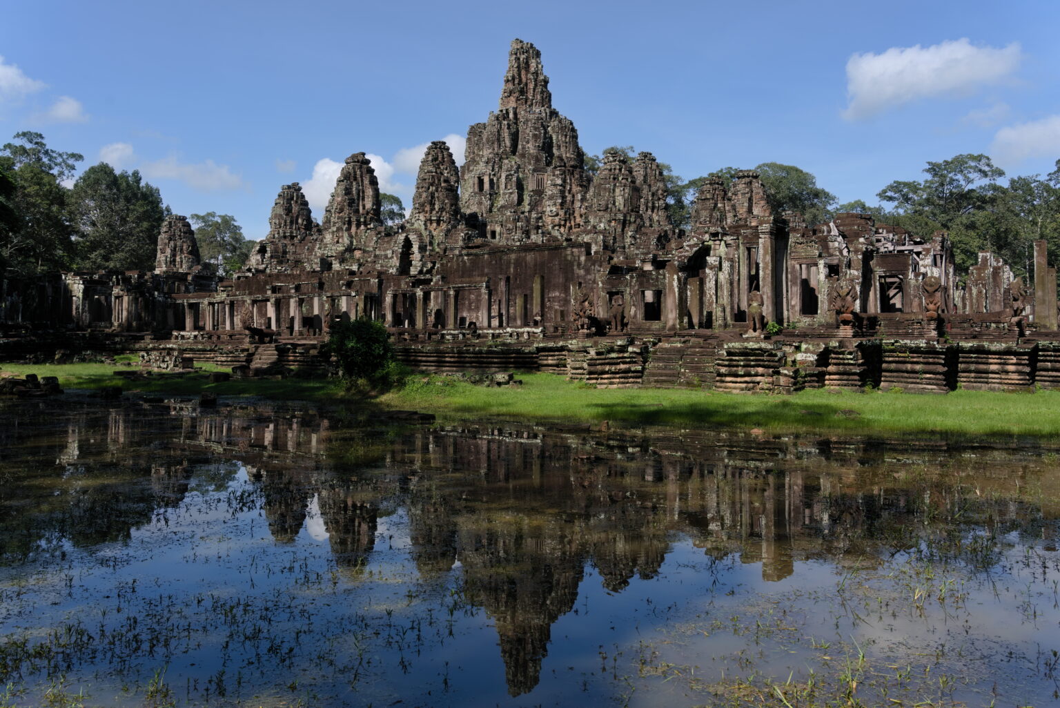 The Bayon temple at Angkor Thom reflected whole in a sheet of still water, grass and trees between