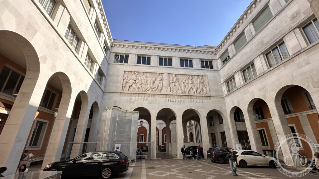 A courtyard with arcades and a large marble relief above Latin inscriptions