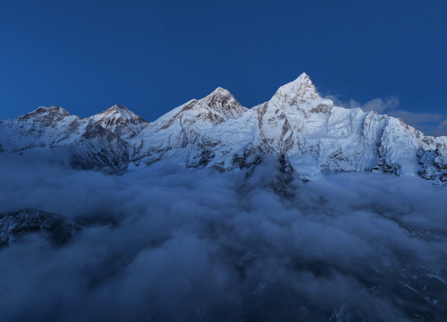 Snow-covered summits of Everest and Nuptse rising above a sea of cloud at dusk