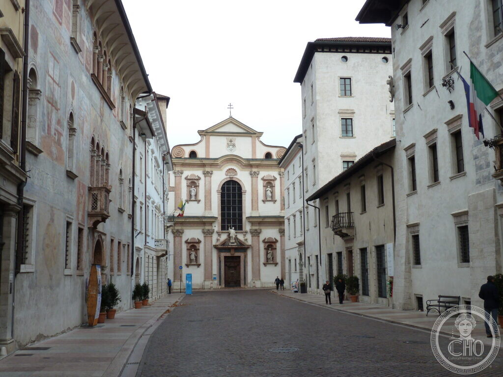 A view down a cobbled street lined with painted buildings, ending at a Baroque church facade.