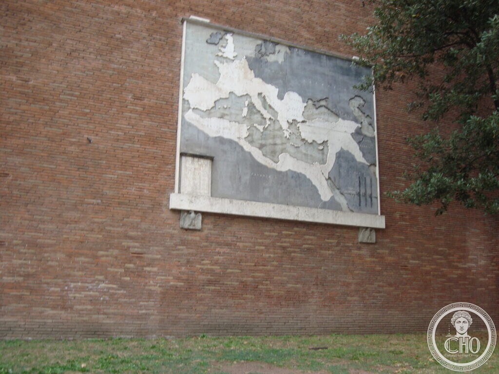A grey marble map on a brick wall with the whole Mediterranean basin, Britain and the Near East inlaid in white, partly shaded by the branches of a tree