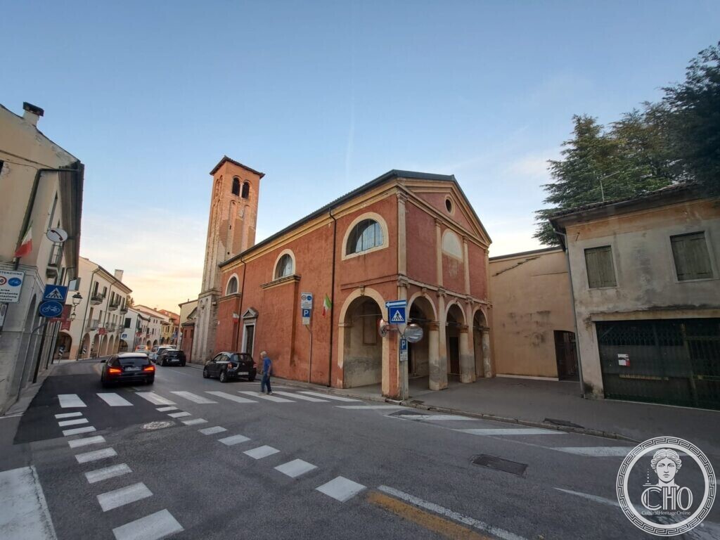 The red church and its brick bell tower seen along the street with a pedestrian crossing in the foreground and houses beyond
