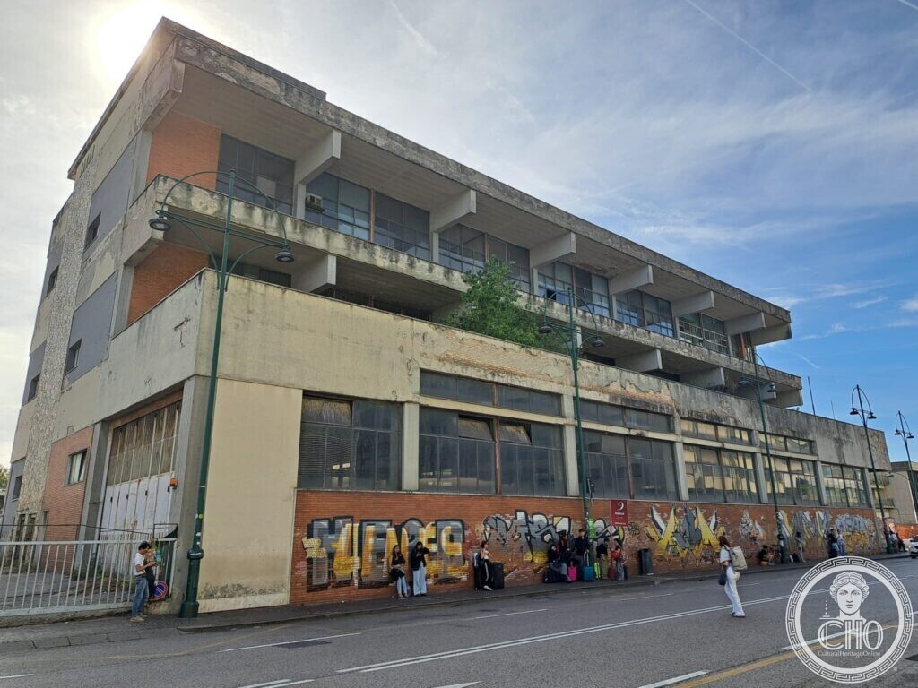 Corner view of the concrete block with its deep balconies, graffiti and people waiting at a bus stop below