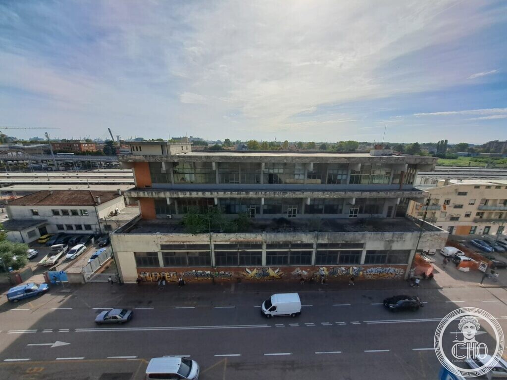 The front of the concrete building seen from above with its bands of windows and graffiti at street level, cars and a van on the road