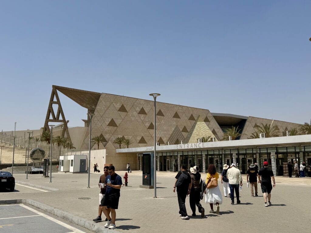 The translucent stone facade of the Grand Egyptian Museum at Giza, a long wall of triangular panels