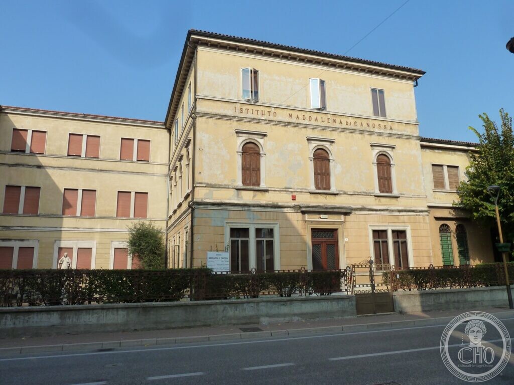 A three-storey pale yellow corner building with round-arched windows on the first floor, the inscription Istituto Maddalena di Canossa on the front, a lower wing along the street, an iron fence and a statue in the garden