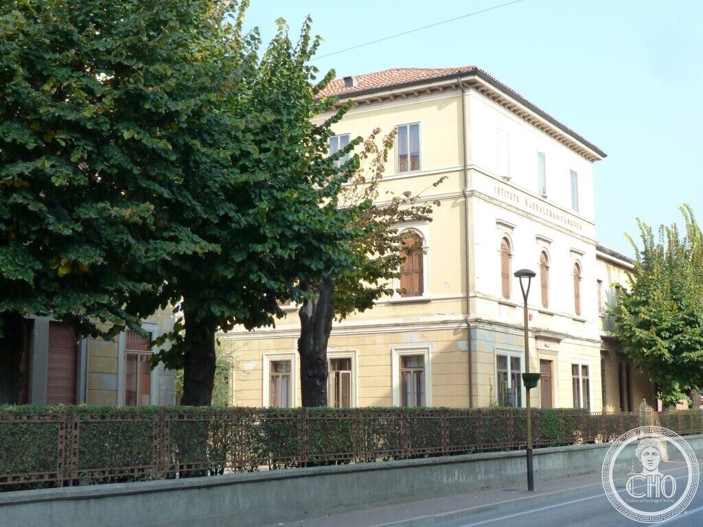 The same yellow building seen from the street through the trees, with the inscription Istituto Maddalena di Canossa on the upper floor and a lamp post in front