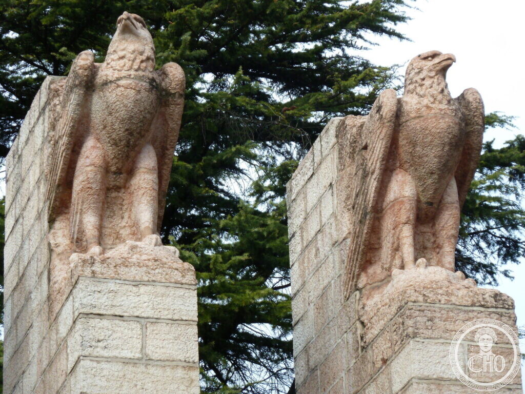 Close-up of two eagle sculptures atop stone pillars against evergreen trees.