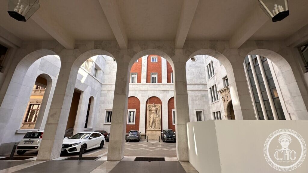 A view through stone arches toward a courtyard with a statue and cars