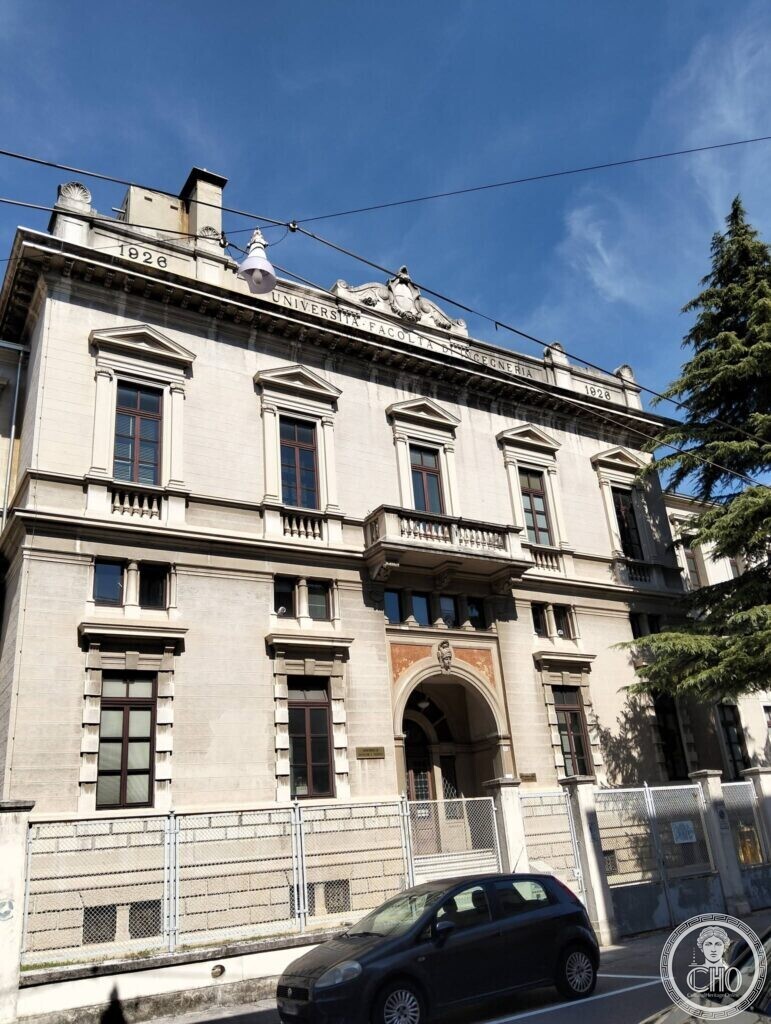 Upward view of a two-storey wing with pedimented windows, a central balcony and an arched entrance; the attic carries the inscription Università Facoltà di Ingegneria with the date 1926 at both ends