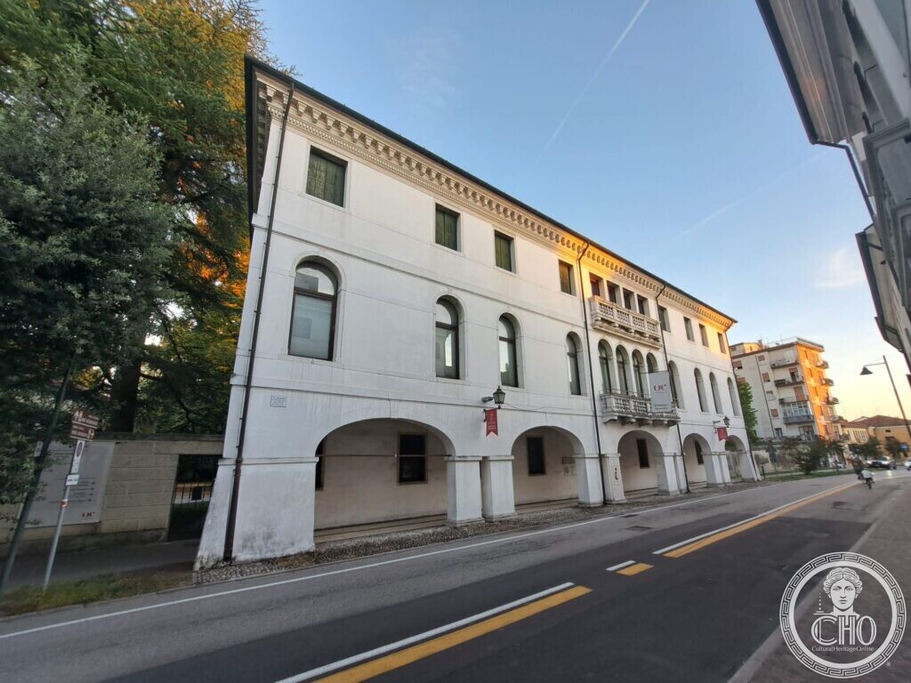 The white palace with its arcade and balcony seen from the east along the street, the upper floor lit by the sunset