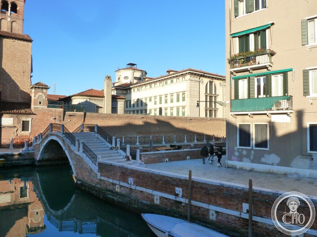 The same stone bridge seen from the other bank, with a green lamp post and a souvenir kiosk in the foreground and old houses with Gothic windows behind