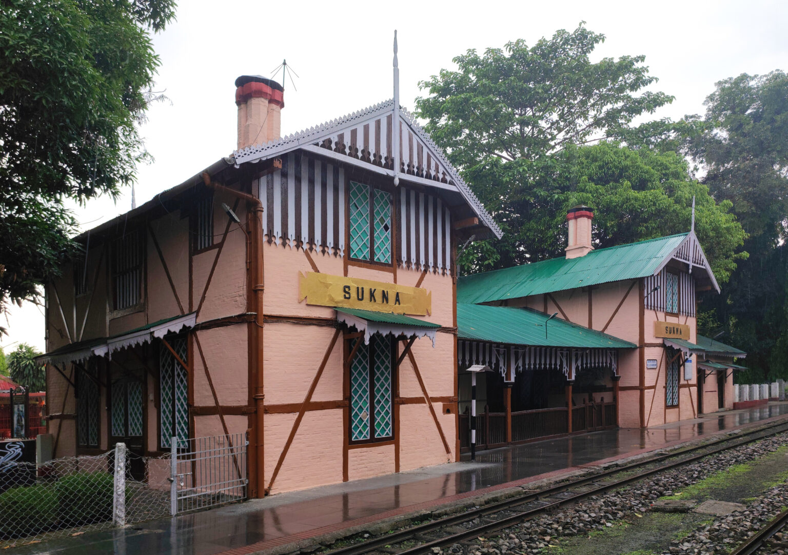 A small timber station building with a pitched roof and a platform sign reading Sukna